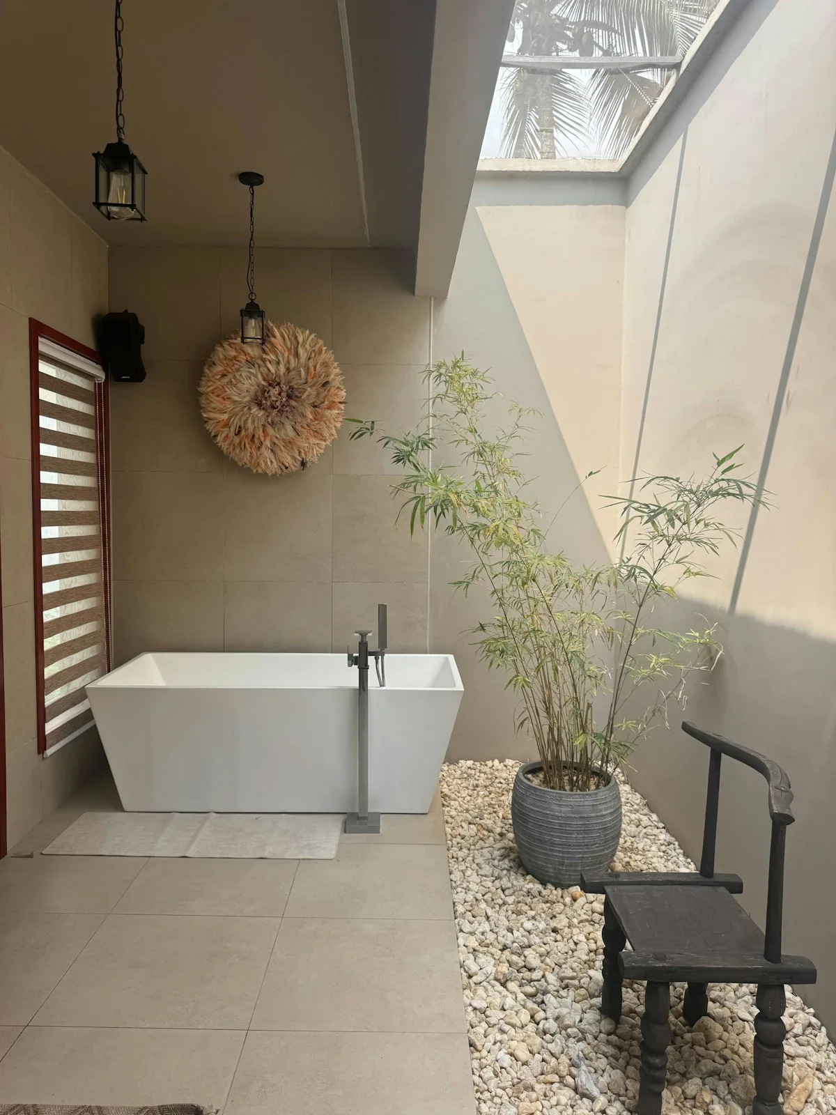 An open-air bathroom with a rectangular bathtub, bamboo plant, pebbles, and natural skylight