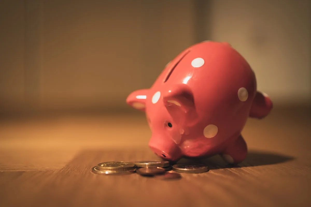 A pink polka-dot piggy bank tipped over with coins spilling out on a wooden surface