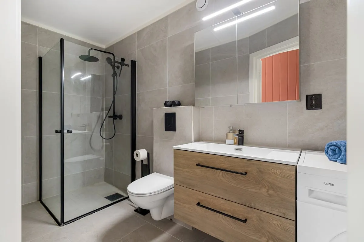 A clean modern bathroom with a wall-hung toilet next to a walk-in shower and floating wood vanity