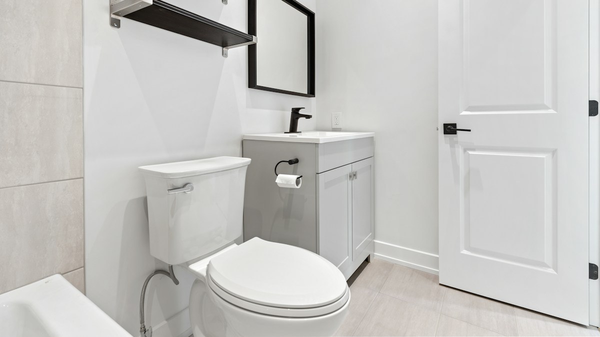 A clean white bathroom with an elongated toilet next to a grey vanity and a black-framed mirror